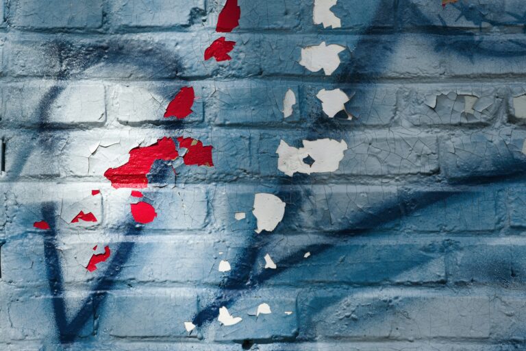 Blue brick wall with peeling paint and graffiti.