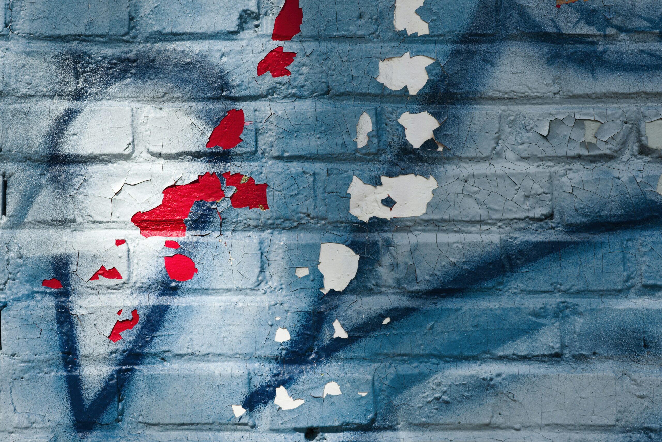 Blue brick wall with peeling paint and graffiti.