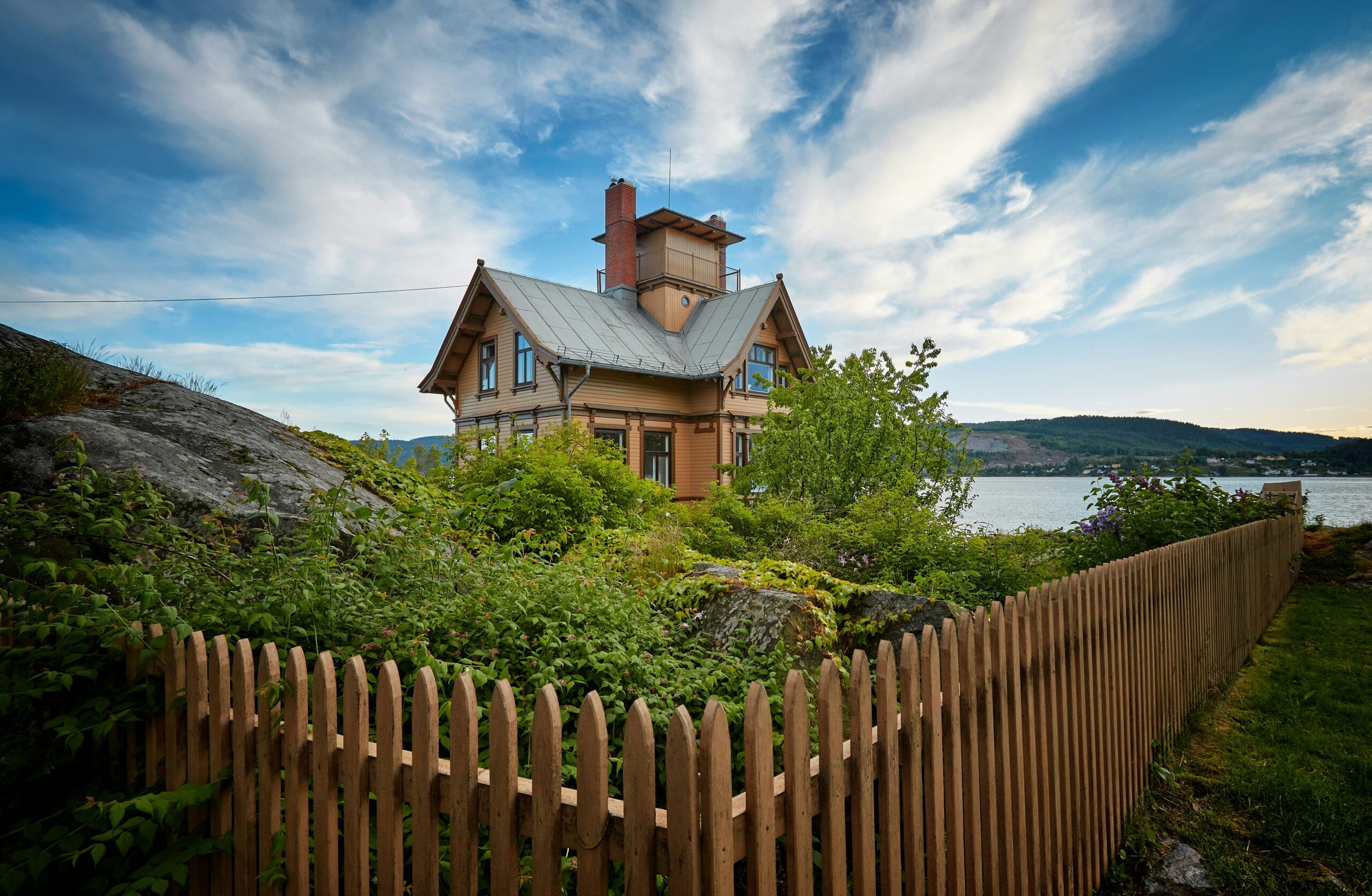 brown wooden house surrounded by fence near body of water