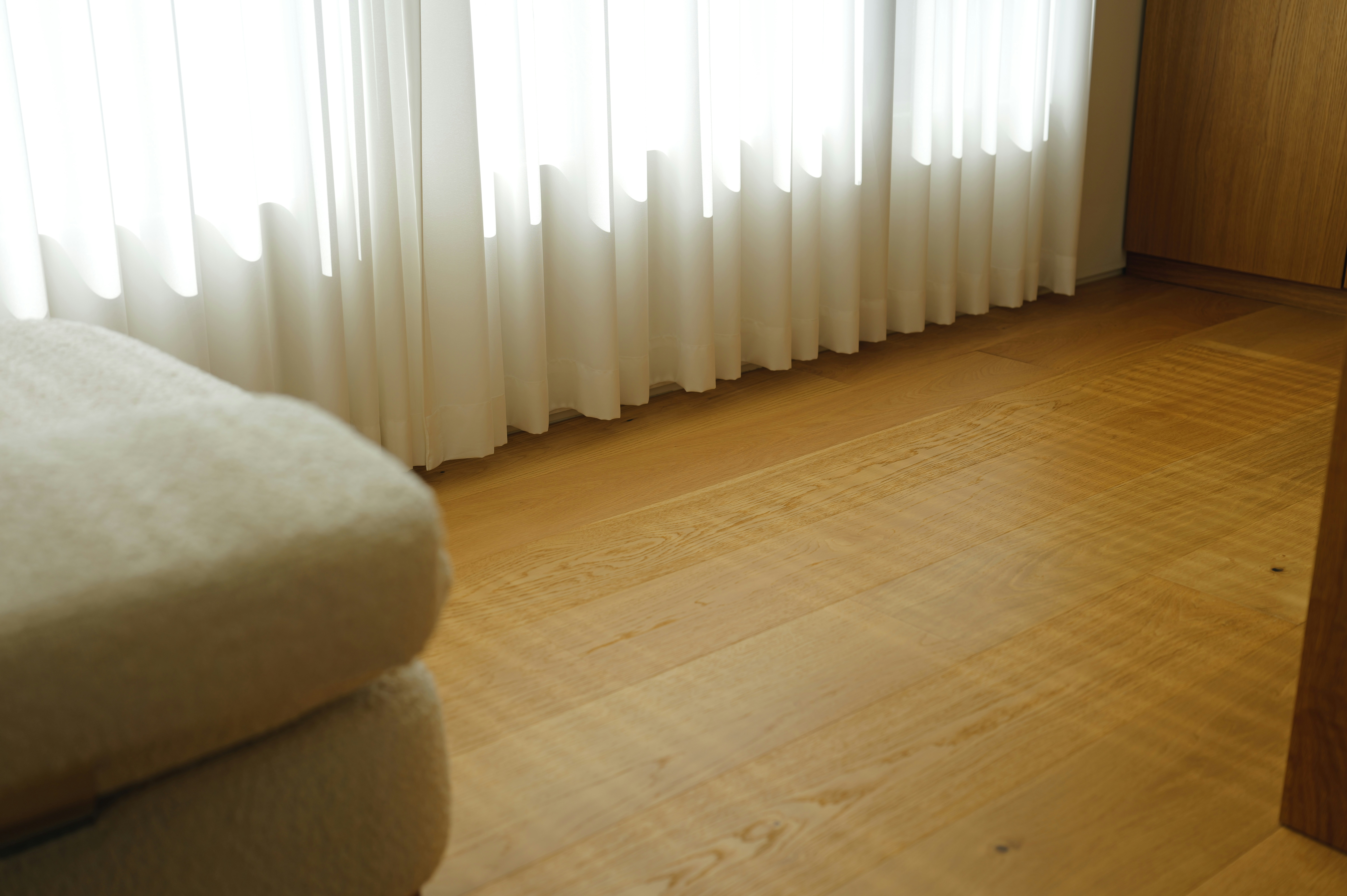 A bed and wooden floor near a window with curtains